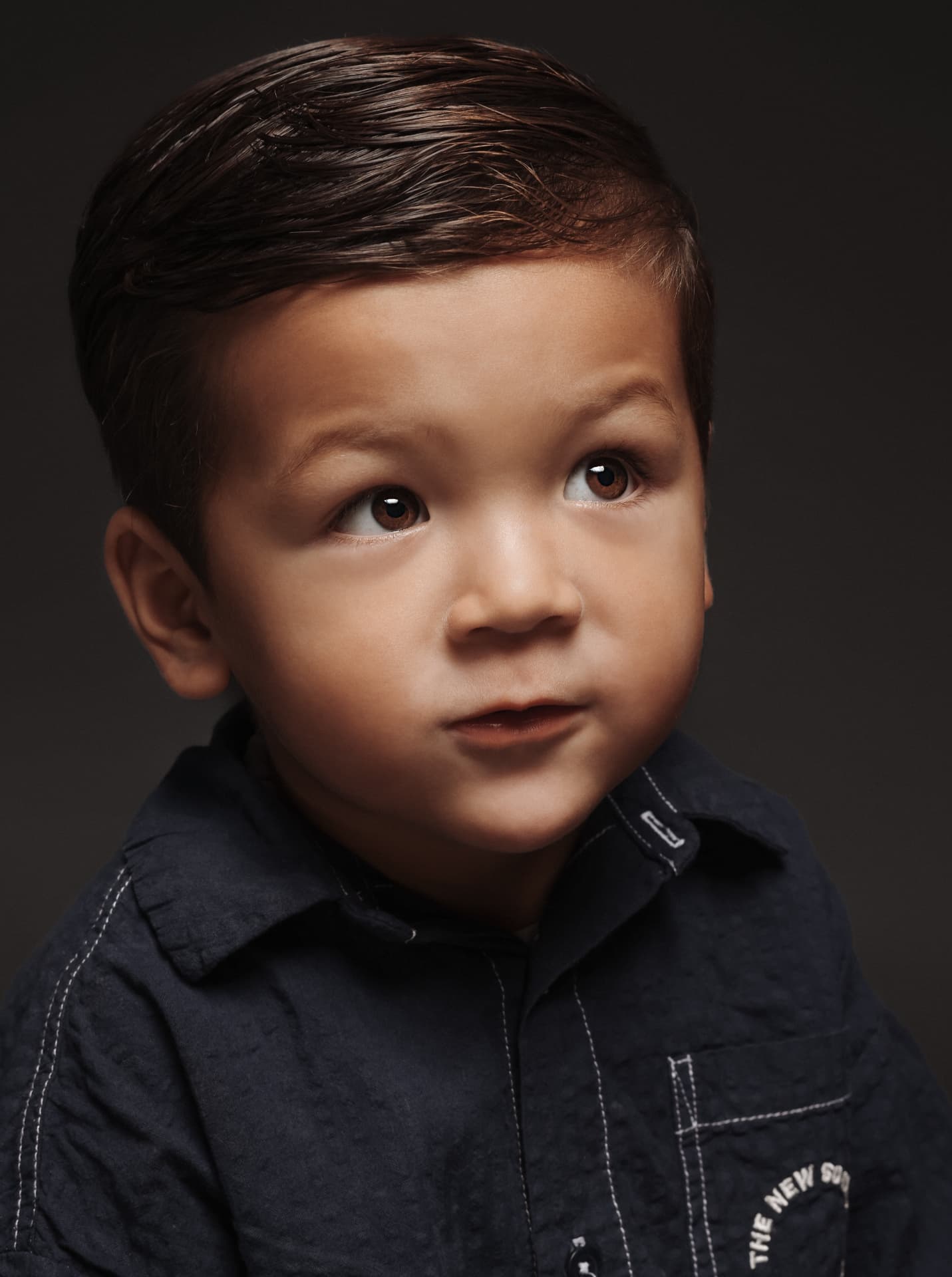 Portret van een jongen in een donker overhemd tegen een donkere achtergrond
